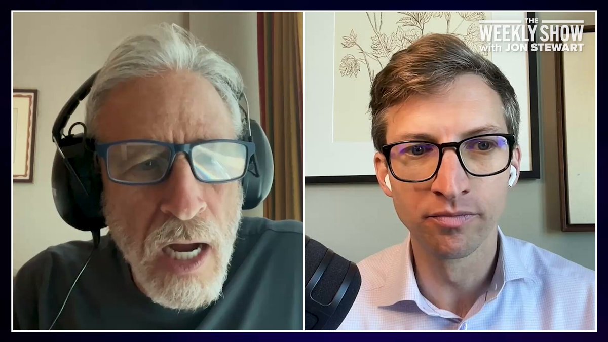 Split-screen video interview: left is an older man with gray hair and a beard wearing headphones; right is a younger man with glasses and wireless earbuds, a microphone between them. The talk show branding appears in the top-right corner.