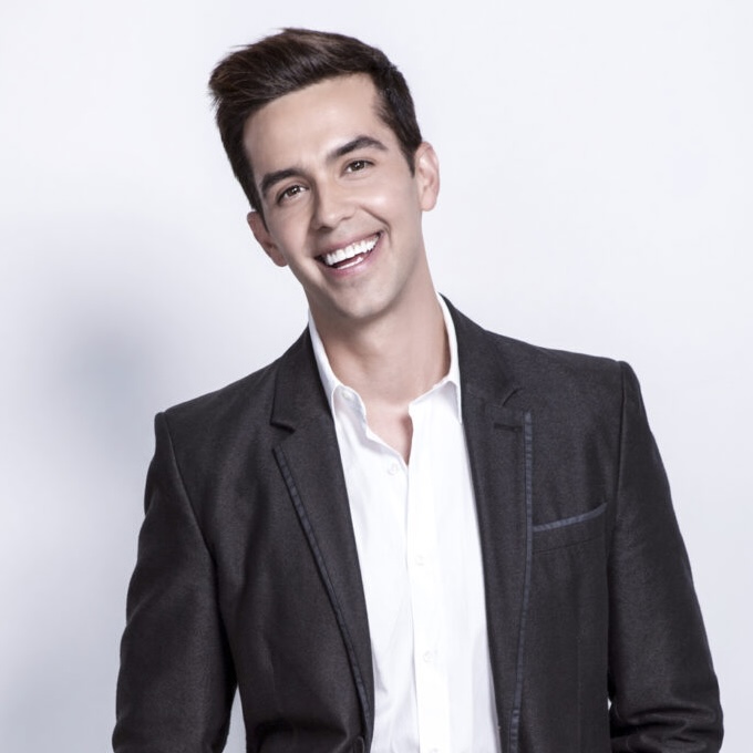 Smiling man in a dark blazer and white shirt posing for a headshot in a studio setting.
