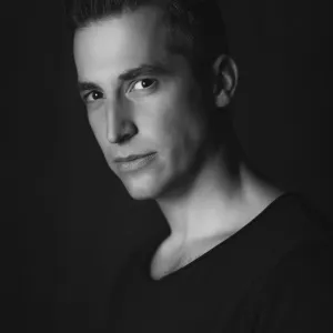 Black-and-white portrait of a man with short dark hair, looking at the camera against a dark background.
