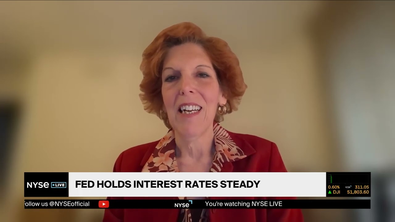 Woman in a red blazer speaks on a live news broadcast about the Fed holding interest rates steady.