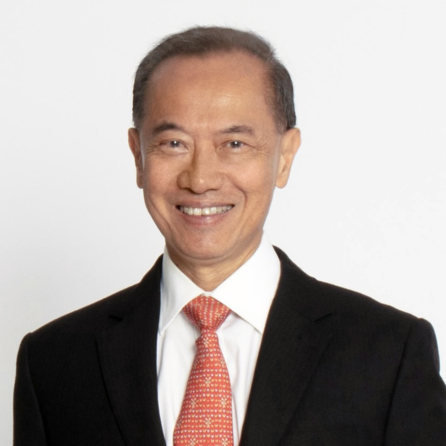 Smiling Asian man in a black suit and red patterned tie against a white background (professional headshot).