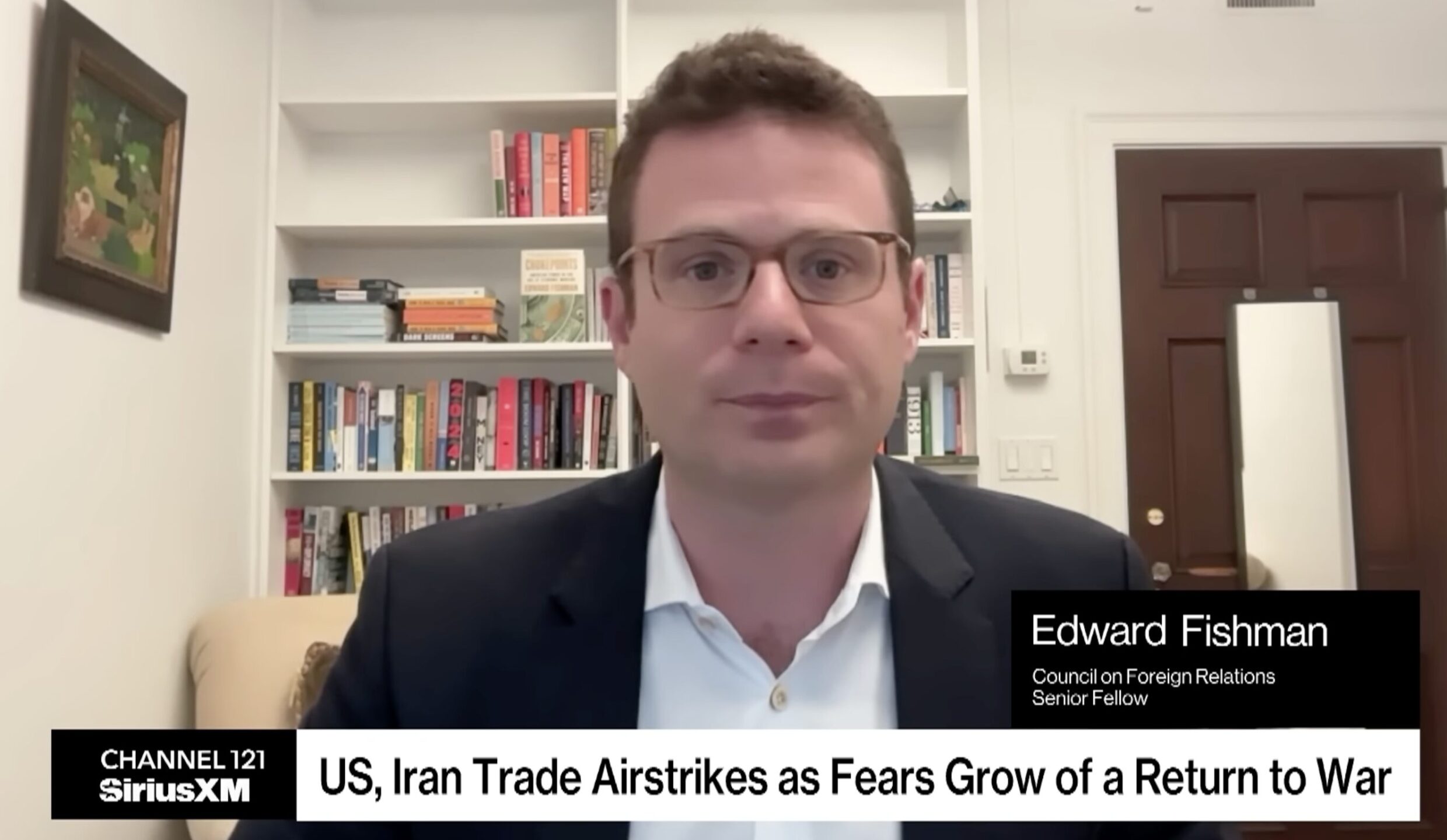 Close-up of Edward Fishman speaking in a video interview, bookshelf background visible behind him, name badge on screen reading 'Edward Fishman'.