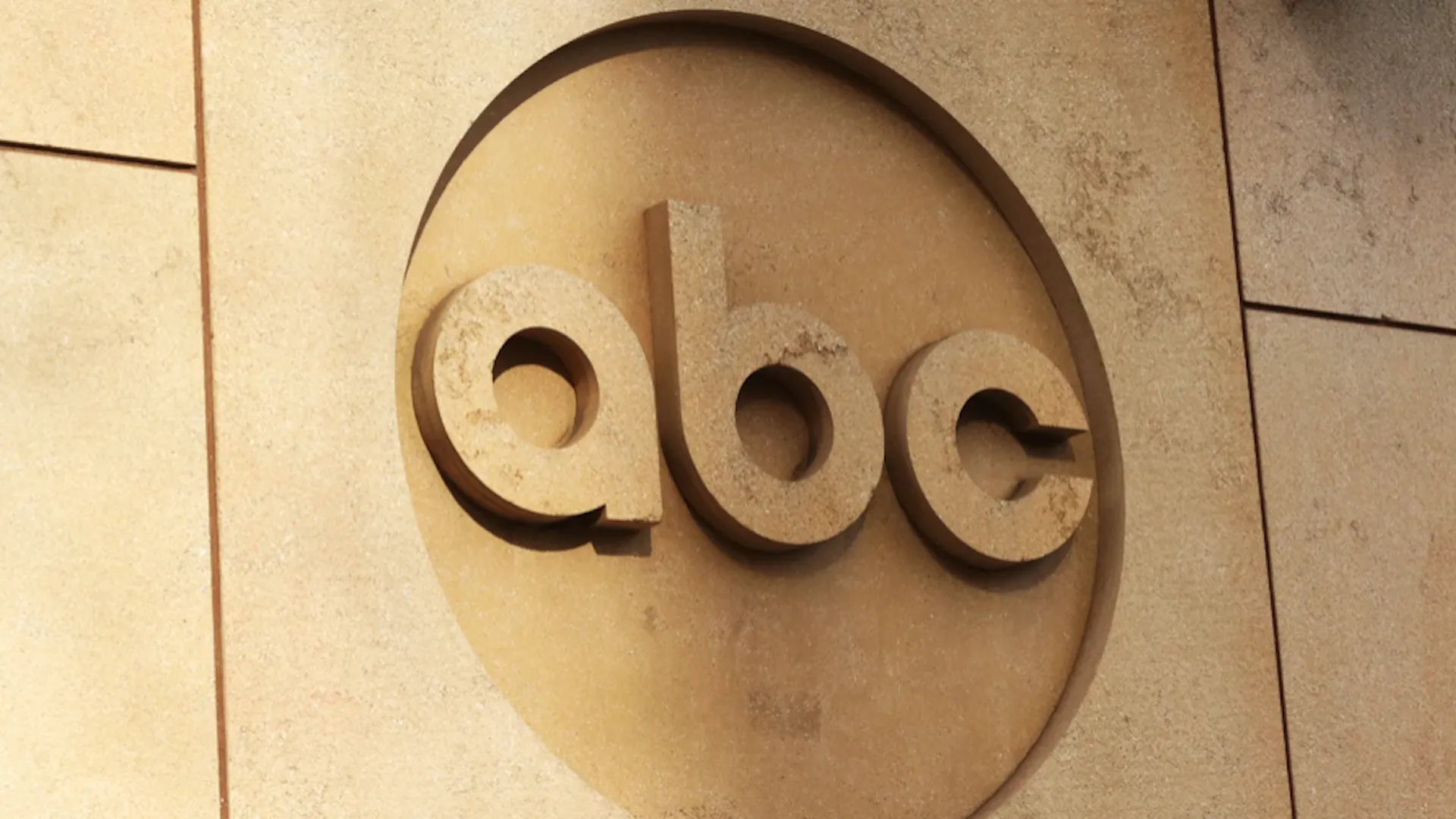 Circular stone plaque with the carved letters “eoe” in relief on a beige textured wall