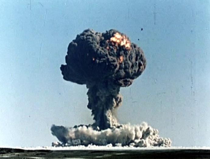 Nuclear explosion with a large mushroom cloud rising from the ground over a flat landscape.